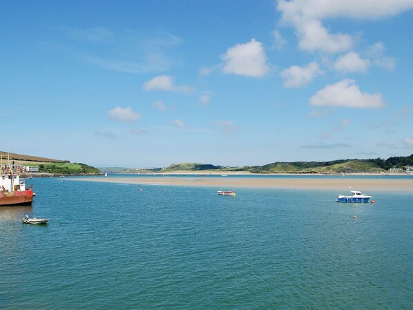 A coastal scene with calm waters, boats, and a hilly landscape in the background.