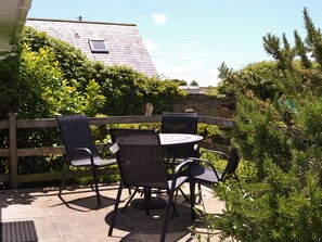An outdoor patio with a round table and four chairs, surrounded by greenery and a wooden fence.