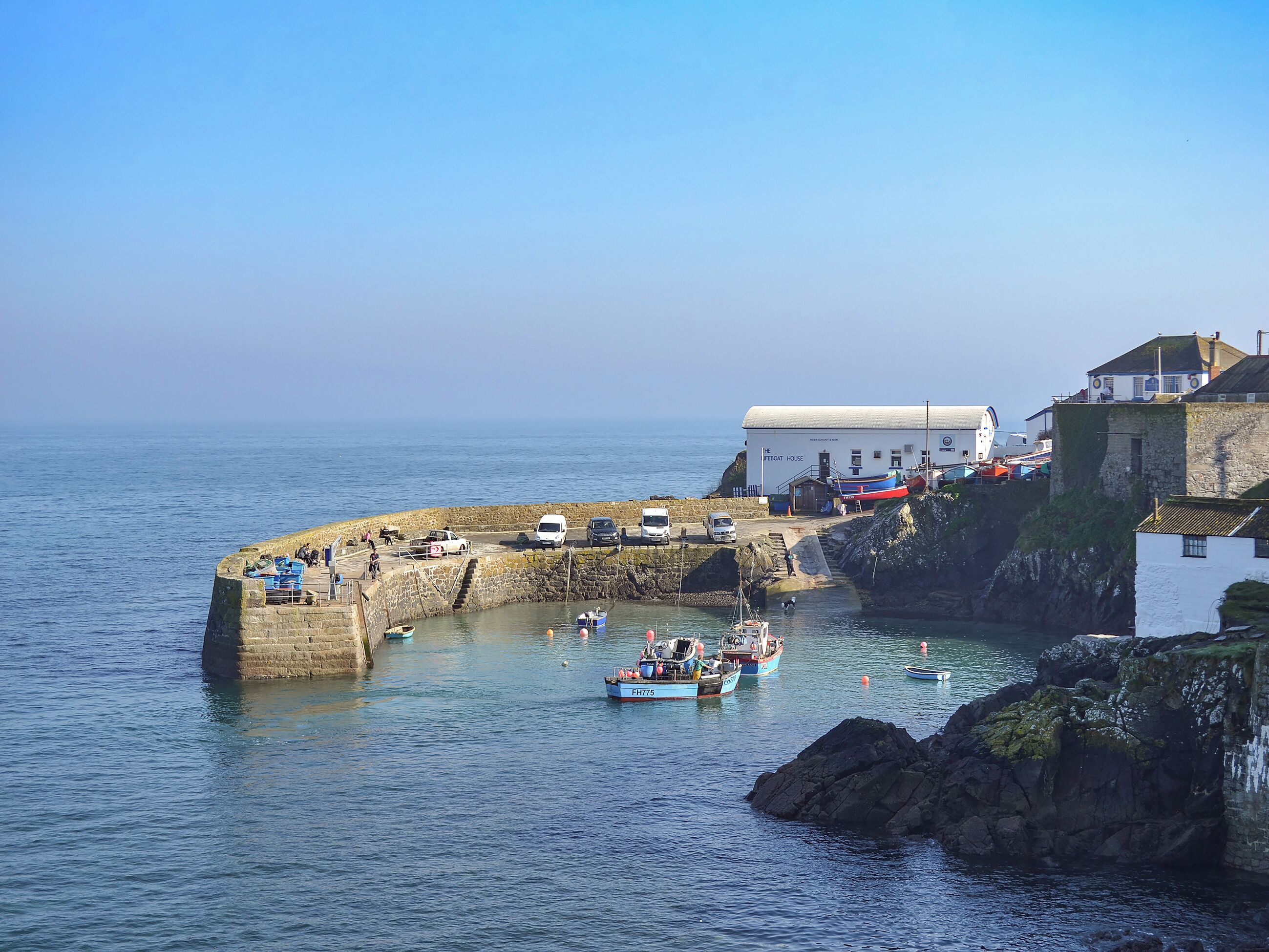 A coastal area with a stone pier, boats, and a building labeled 'The Boat House.'