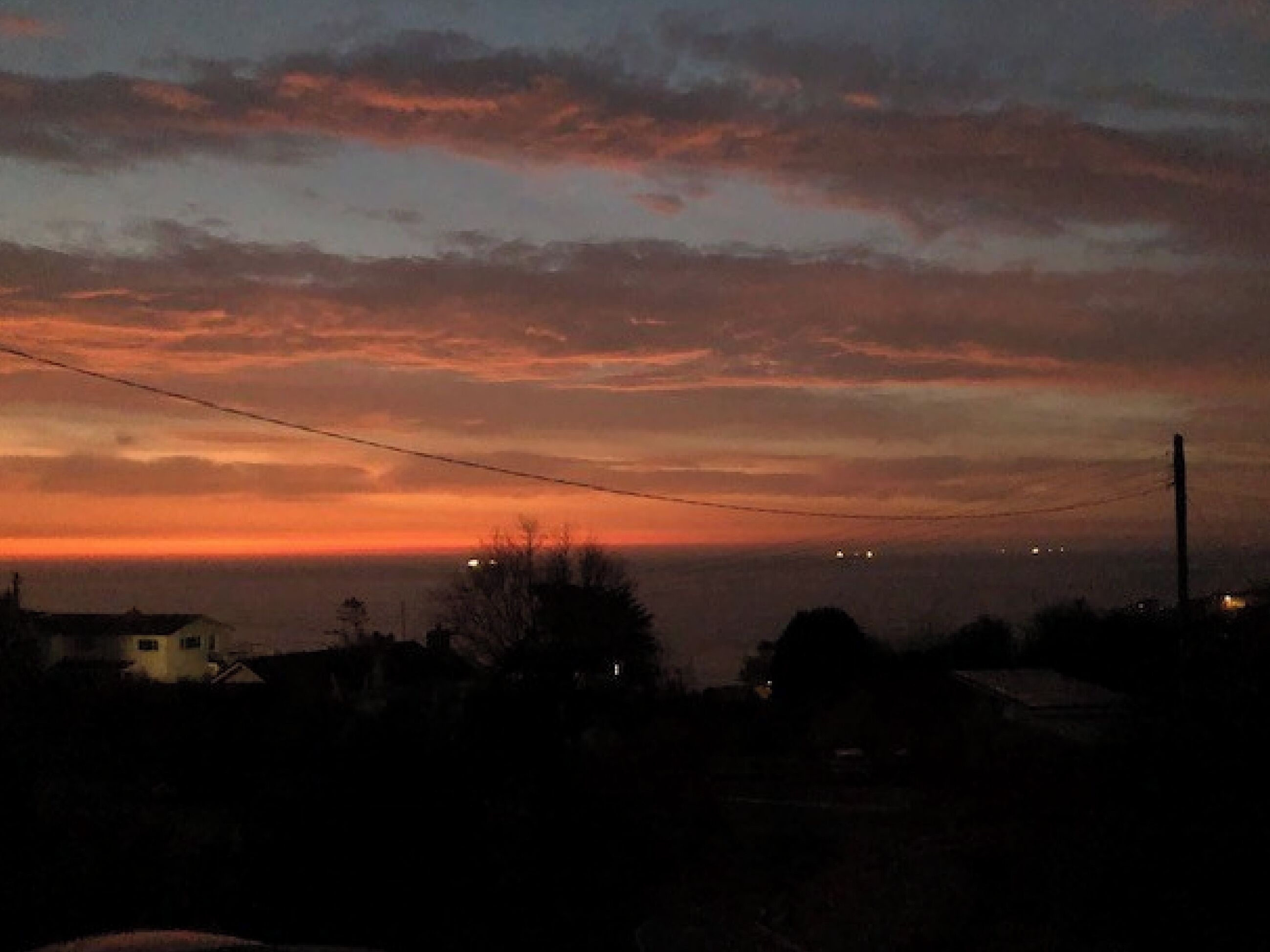 Een zonsondergang boven een woonwijk met huizen en elektriciteitsleidingen.
