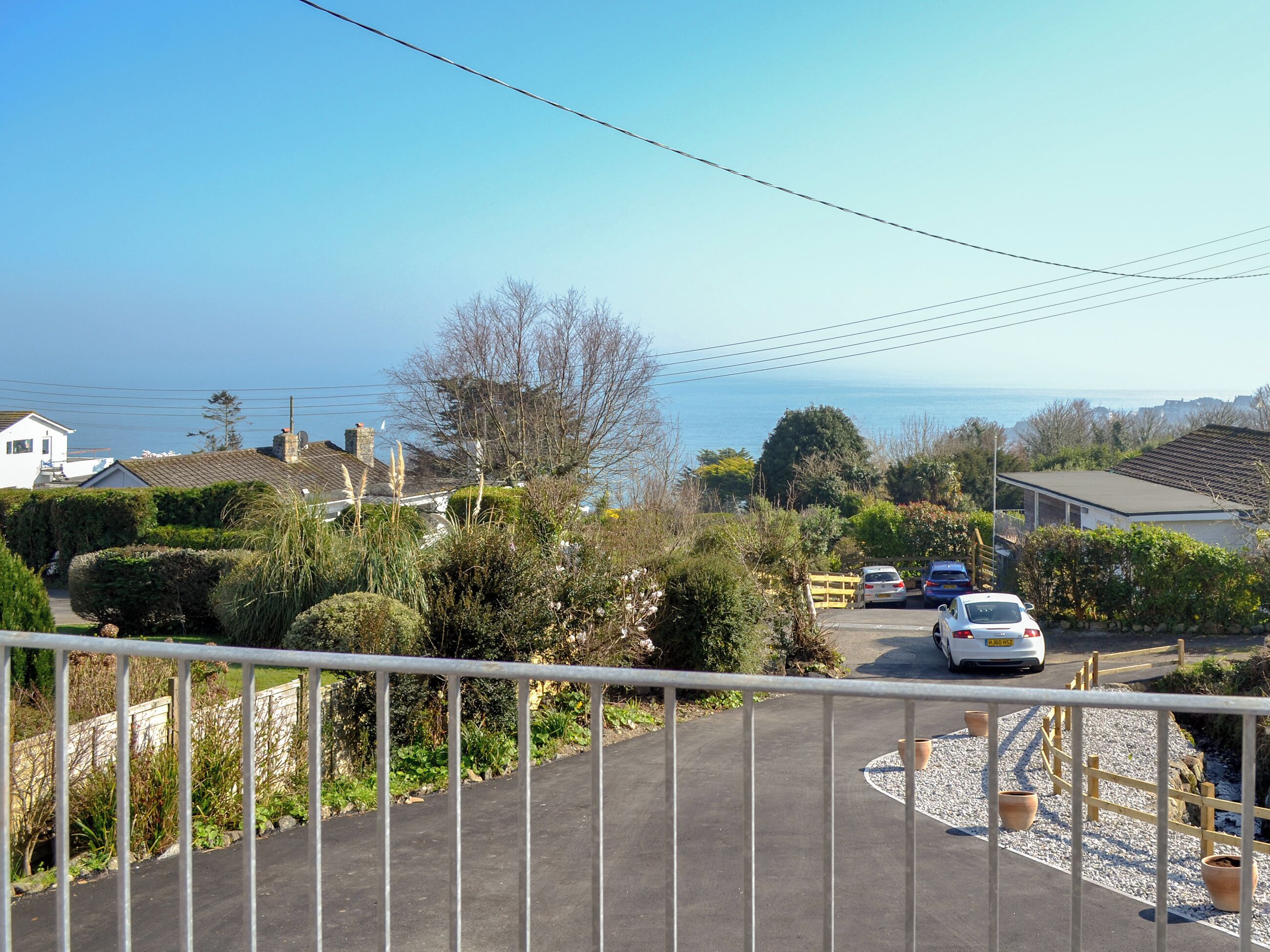 A residential area with a paved driveway, parked cars, and a view of the sea.