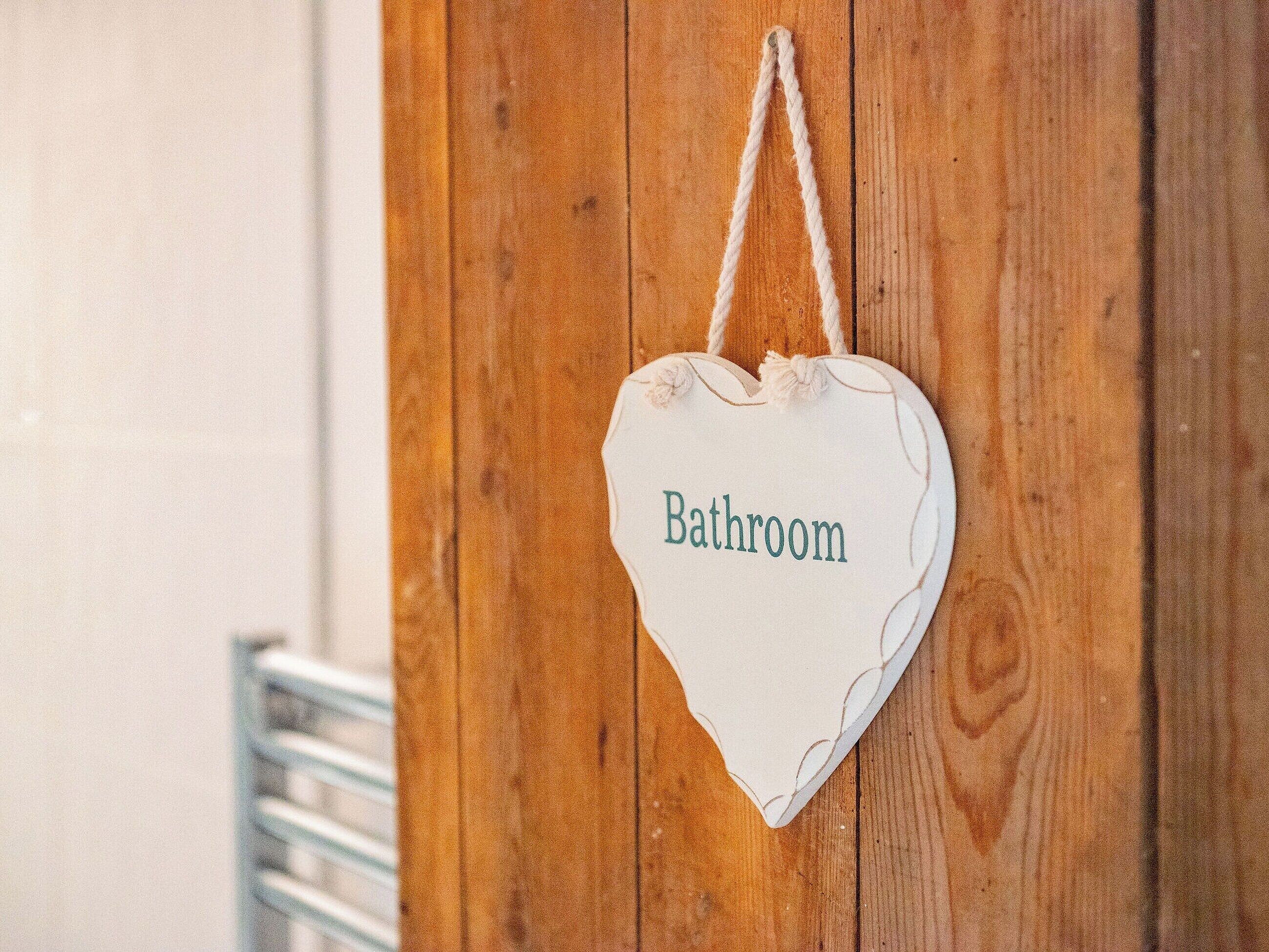 A heart-shaped sign with the word "Bathroom" hanging on a wooden door.