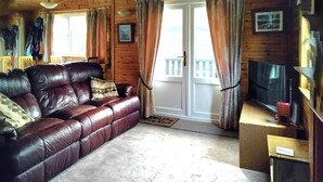 A cozy living room with a leather sofa, a television, and wooden walls. - 3 bedroom accommodation in Keswick (Keswick)