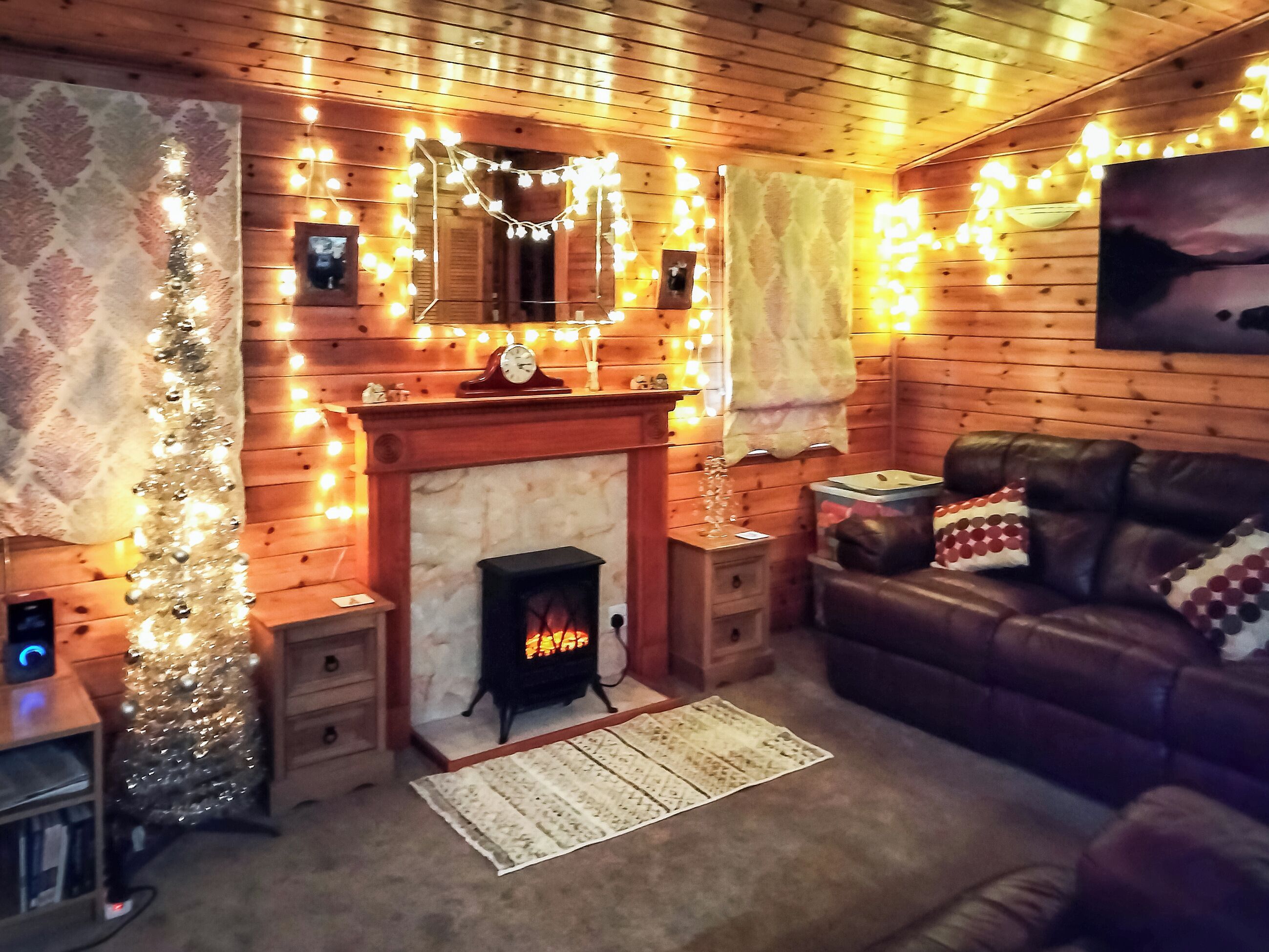 A cozy room with a fireplace, wooden walls, a leather sofa, and string lights.