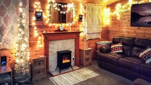 A cozy room with a fireplace, wooden walls, a leather sofa, and string lights. - 3 bedroom accommodation in Keswick (Keswick)
