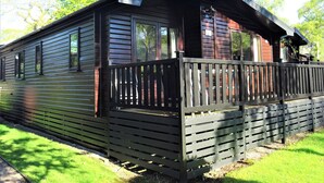 A cabin with a wooden exterior, a porch with a railing, and a window overlooking a grassy area. - 3 bedroom accommodation in Keswick (Keswick)