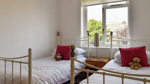 Une chambre avec deux lits simples, une table de chevet, une lampe et une fenêtre donnant sur les arbres.