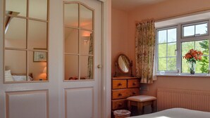 A bedroom with a bed, a dresser, a mirror, a window with curtains, and a radiator. - 3 bedroom accommodation in Oldcroft, Lydney (Oldcroft, Lydney)
