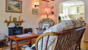 A cozy living room with a wooden table, floral armchair, and a fireplace. - 3 bedroom accommodation in Oldcroft, Lydney (Oldcroft, Lydney)