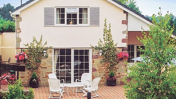 A two-story house with a large front window and shutters, a patio with white chairs, and potted plants. - 3 bedroom accommodation in Oldcroft, Lydney (Oldcroft, Lydney)