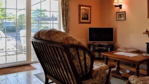 A living room with a wooden ceiling, a television, a fireplace, and a large window with a view of the outside. - 3 bedroom accommodation in Oldcroft, Lydney (Oldcroft, Lydney)