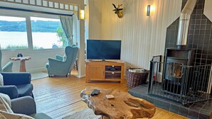A cozy living room with a wooden coffee table, a television, a fireplace, and a view of the outdoors. - 2 bedroom accommodation in Ardentinny near Dunoon (Ardentinny near Dunoon)