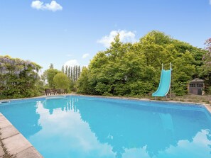 Ein klares, blaues Schwimmbecken mit Rutsche, umgeben von üppigem Grün und Bäumen.