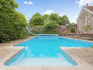 Ein rechteckiger Swimmingpool mit blauer Fliesenbordur, einer Rutsche und einer Steinmauer im Hintergrund.