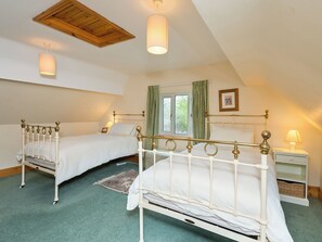 A bedroom with two single beds, a wooden ceiling, a window with curtains, and a bedside table with a lamp. - 3 bedroom accommodation in Wareham (Wareham)