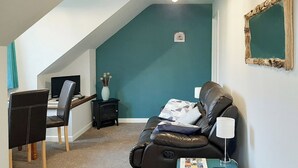Ein Wohnzimmer mit einem schwarzen Ledersofa, einem kleinen Tisch mit Lampe, einem Schreibtisch mit Computer und einer Wand in Türkis.