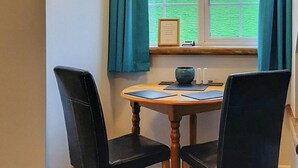 Ein Esstisch mit zwei schwarzen Stühlen, ein Holztisch und ein Fenster mit Vorhängen.