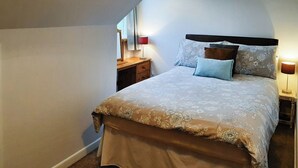 Ein Schlafzimmer mit Bett, Nachttisch, Kommode und Fenster.