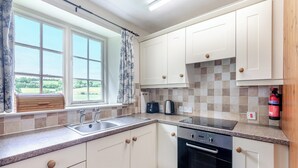 A kitchen with white cabinets, a built-in oven, a sink, and a window with curtains. - Stable Cottage - 26032 (Wark, near Hexham)