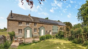 A stone house with a green door, a small garden, and solar panels on the roof. - Stable Cottage - 26032 (Wark, near Hexham)