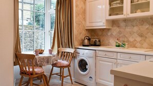 A kitchen with a washing machine, a table with chairs, and a window with curtains. - 2 bedroom accommodation in Skipton (Skipton)