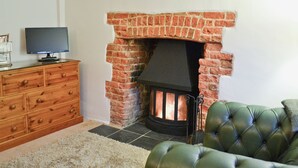 A living room with a brick fireplace, a television on a wooden cabinet, and a green leather sofa.