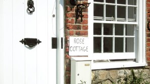 A white door with a black knocker, a sign reading "ROSE COTTAGE", and a white post box labeled "POST".