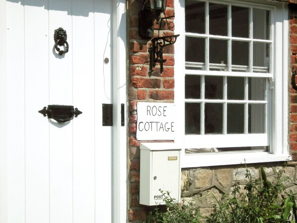 A white door with a black knocker, a sign reading "ROSE COTTAGE", and a white post box labeled "POST".