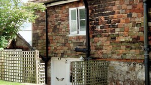 A brick house with a white door, a window, and a metal gate.