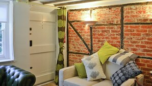 A room with a brick wall, a white door, a green curtain, a leather chair, and a sofa with multiple cushions.