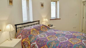 Un dormitorio con una cama, dos mesitas de noche, dos lámparas y dos ventanas con persianas.