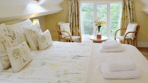 A bedroom with a large bed, two chairs, a small table with a vase, and a window with curtains.