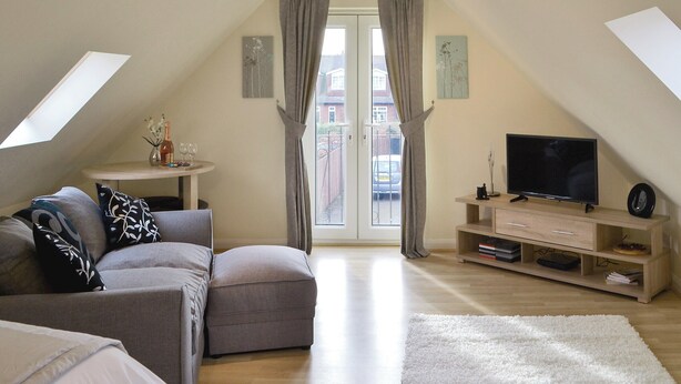 Ein gemütliches Schlafzimmer im Loft-Stil mit einer Couch, einem Fernseher und einem kleinen Tisch mit Vase und Weingläsern.