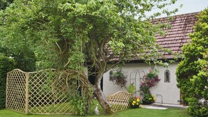 Ein rustikales Haus mit Ziegeldach, Holzzaun und Garten mit Blumen und Baum.