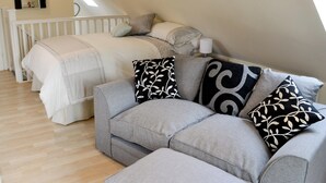 Ein Schlafzimmer mit einem Bett, einem grauen Sofa und einem weißen Geländer.