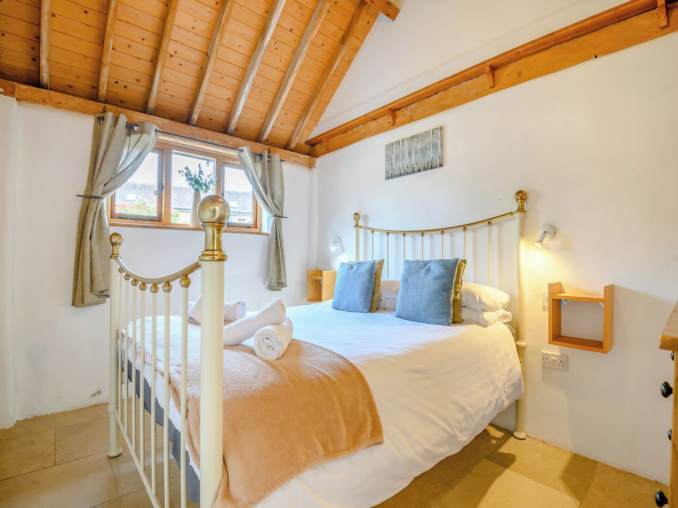 Un dormitorio con cama, cortinas, una ventana, mesita de noche y lámpara fijada a la pared.