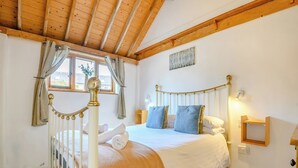Une chambre à coucher avec un lit, des rideaux, une fenêtre, une table de chevet et un luminaire fixé au mur.