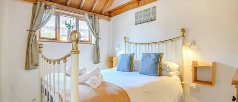 Un dormitorio con cama, cortinas, una ventana, mesita de noche y lámpara fijada a la pared.