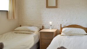 Quarto com duas camas de solteiro, uma mesa de cabeceira com abajur e um espelho na parede.