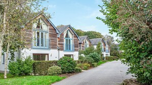 A row of modern houses with pitched roofs, large windows, and blue shutters, surrounded by lush greenery and a paved driveway. - 2 bedroom accommodation in Carnon Downs, near Truro (Carnon Downs, near Truro)