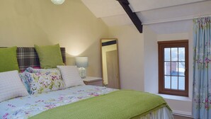 A bedroom with a bed, a nightstand, a lamp, a window with curtains, and a mirror. - A beamed, character cottage situated just 100 yards from the River Teifi. (St Dogmaels near Cardigan)