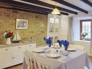 Un coin repas agrémenté d’un mur en pierre, d’un meuble blanc et d’une table mise avec des assiettes, des verres et des serviettes bleues.