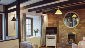 A living room with a fireplace, a television on a stand, and a window with curtains. - A beamed, character cottage situated just 100 yards from the River Teifi. (St Dogmaels near Cardigan)