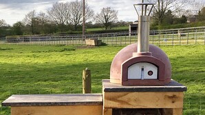 A rustic outdoor seating area with a wooden bench and a brick oven.