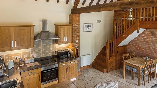 A kitchen with wooden cabinets, a microwave, and a stove. There is a dining area with a table and chairs, and a staircase leading to an upper level.