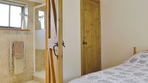 A bedroom with a wooden door, a bed with a patterned bedspread, a window with a view, and a bathroom with a shower and towel rack.