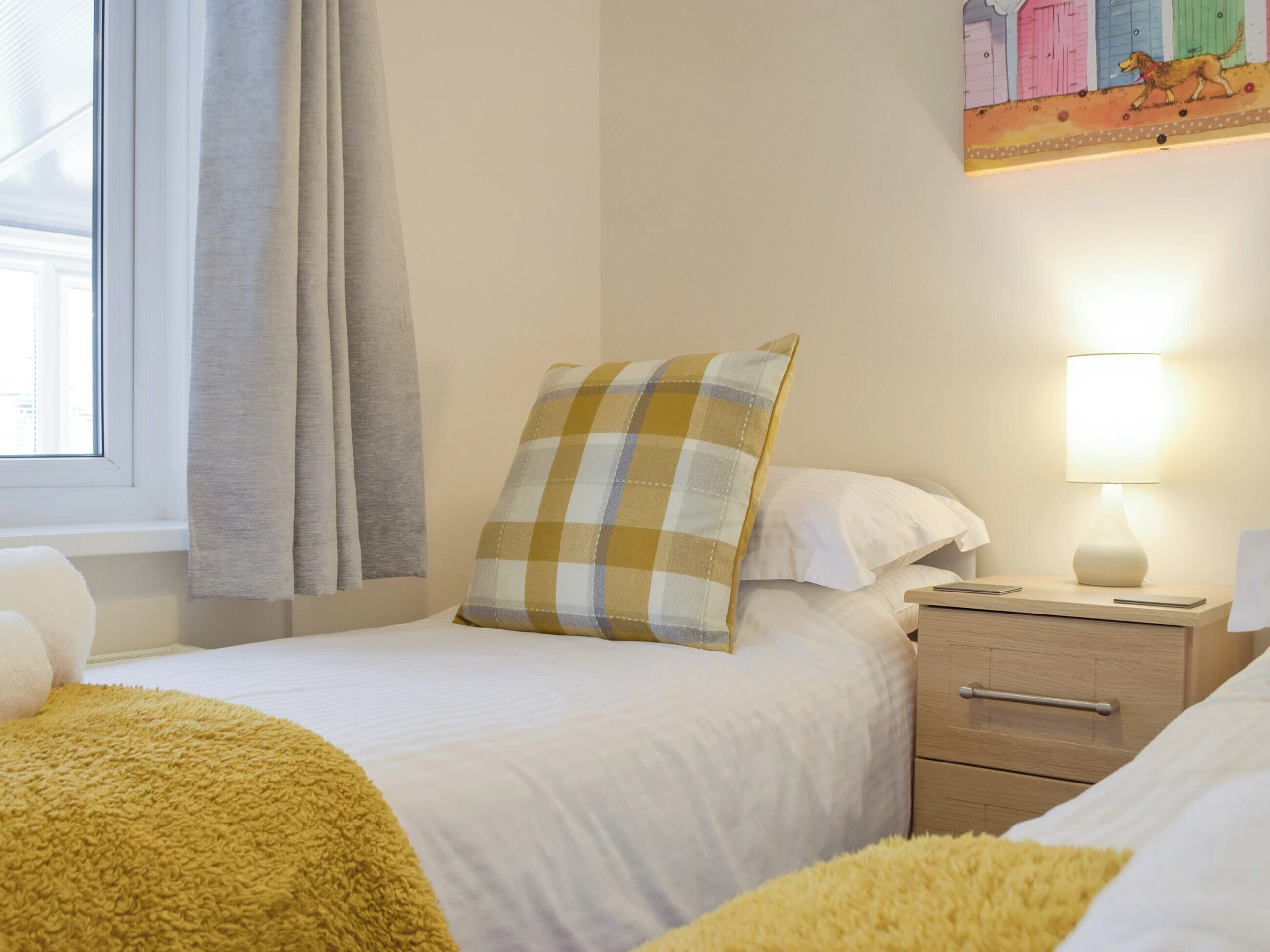 A bedroom with two beds, a bedside table, a lamp, and a window with curtains.