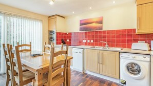 A compact kitchen with wooden cabinets, a built-in oven, a washing machine, and a dining area with wooden chairs and a table. - Super location within woodland and a SSSI. (Glenridding, near Penrith)