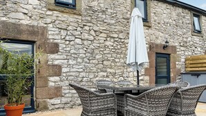 A stone building with a patio featuring wicker furniture and a white umbrella. - Honeysuckle Cottage - 27880 (Matlock)