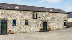 A stone building with multiple windows and doors, a sloped roof, and a gravel driveway. - Honeysuckle Cottage - 27880 (Matlock)